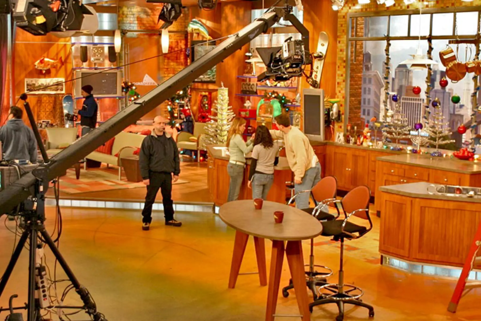 A brightly lit television studio with a large crane camera, wooden set pieces, and festive decorations, preparing for a show A brightly lit television studio with a large crane camera, wooden set pieces, and festive decorations, preparing for a show